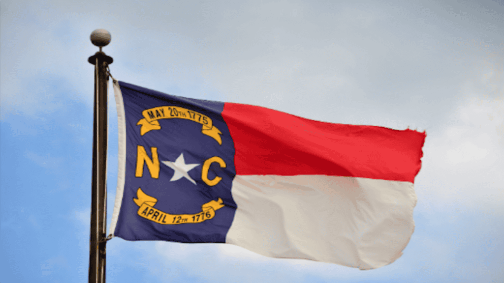 North Carolina state flag waving in the wind against a cloudy sky.