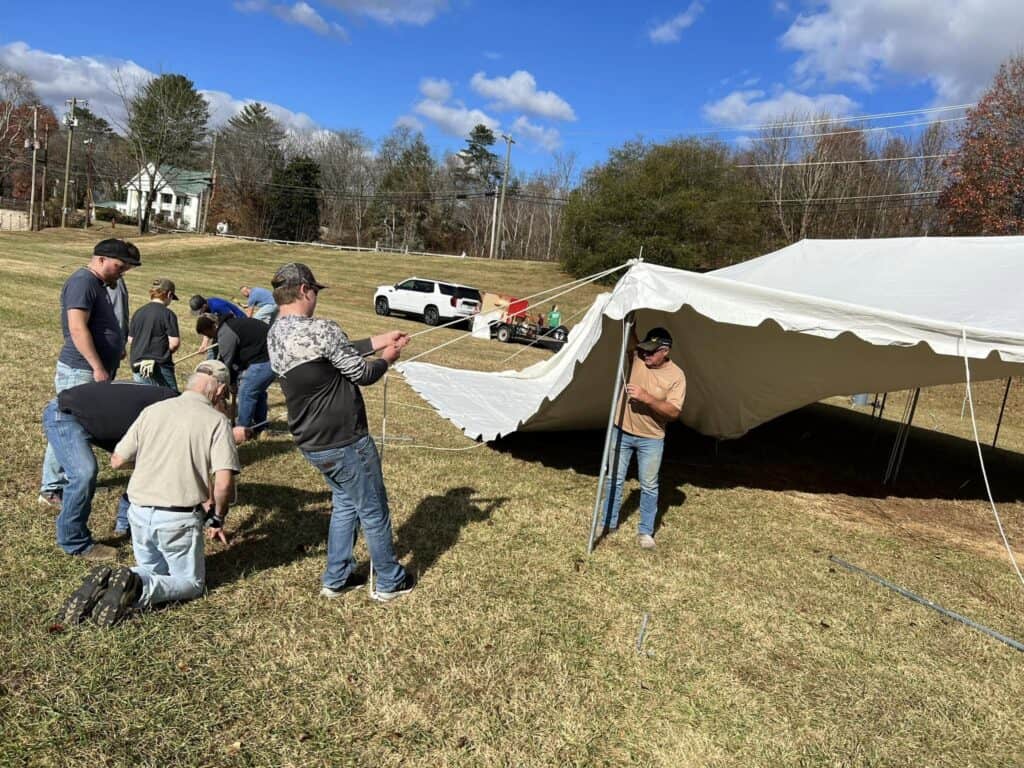 Group assembling a large tent outdoors during daytime event.