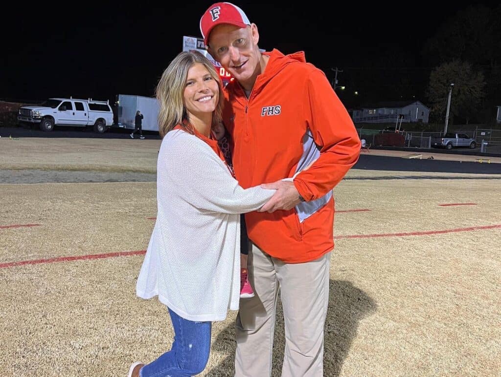 FHS football coach and a woman smiling and embracing on the field after the game.