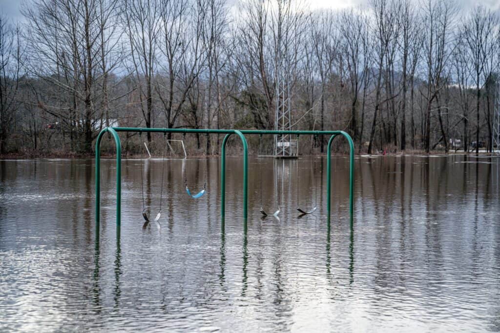 Flooded playground with swings submerged in water after heavy winter rain.