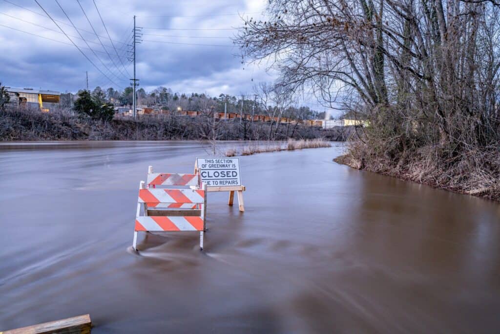 Flooded road in Macon due to heavy winter rain, with barriers and closed signs.