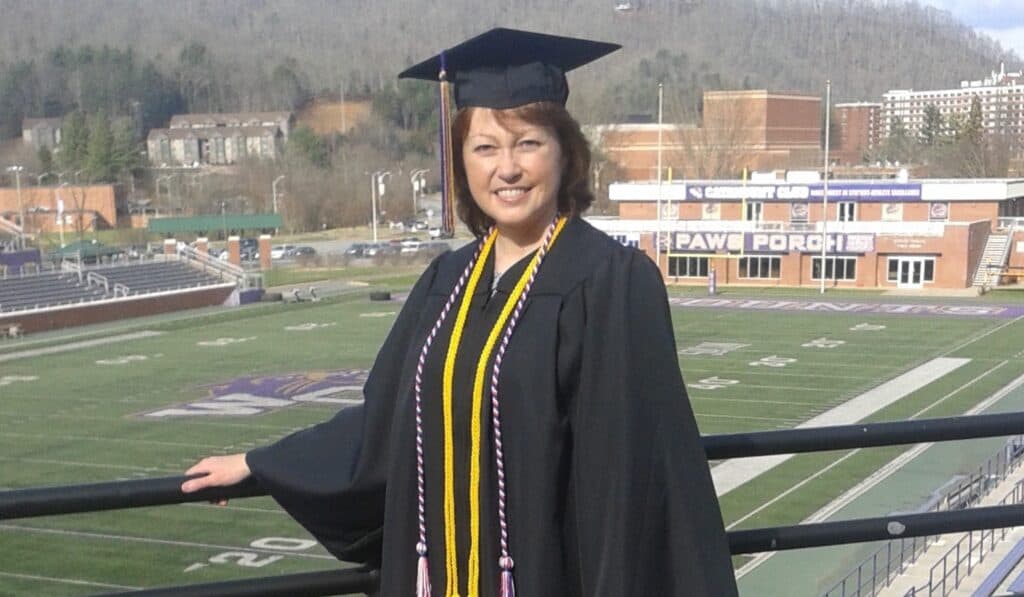 Graduate in cap and gown celebrating at WCU football field.