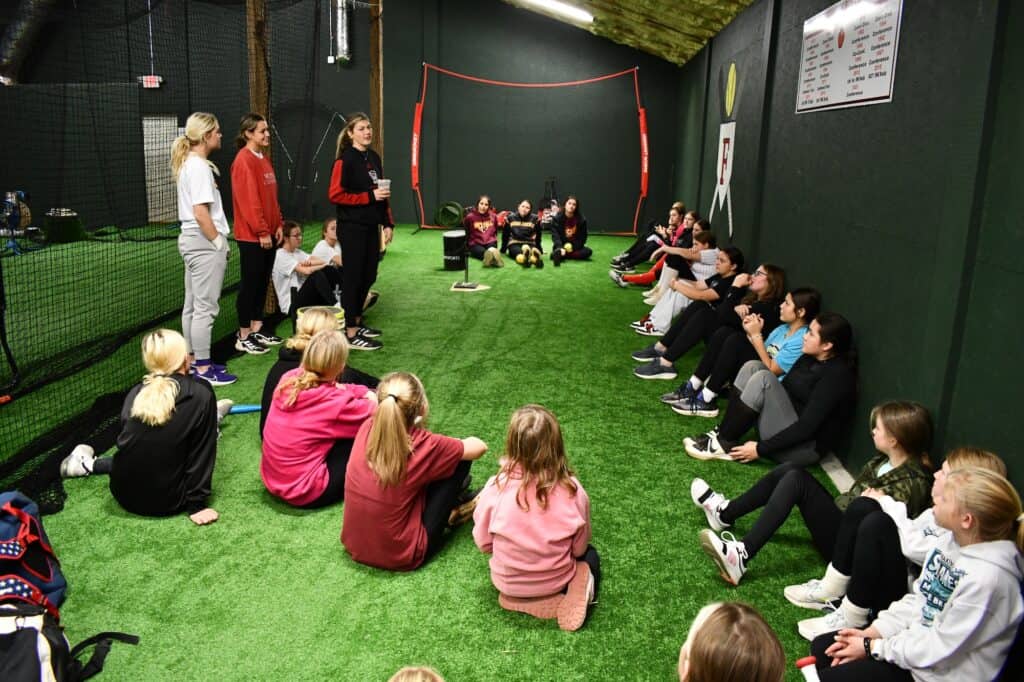 Former FHS softball players sharing college athletic experiences in indoor training session.