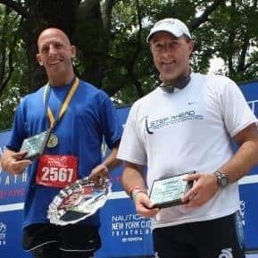 Two men at a community event, one holding a medal and the other a plaque, promoting local engagement.