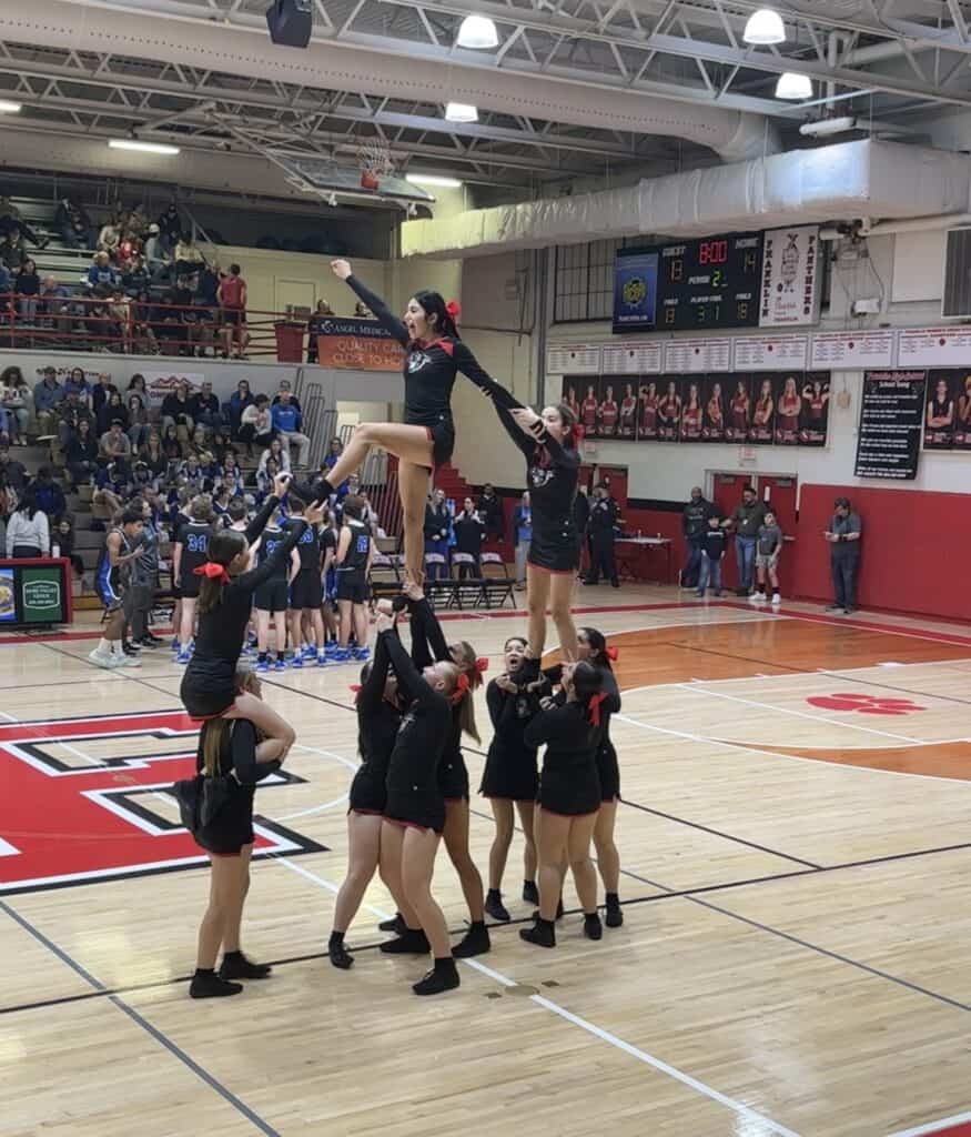 Cheerleaders performing a stunt during a basketball game at a gymnasium.
