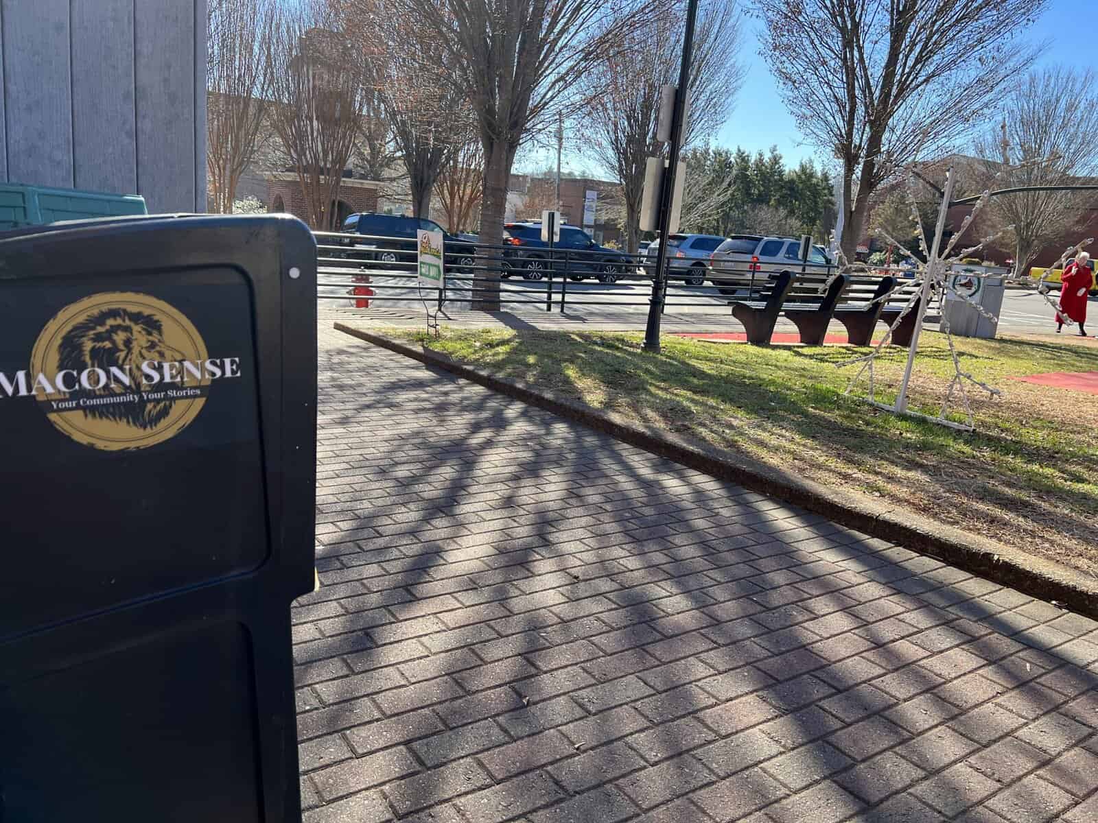 Macon Sense sign in a park with benches and trees.