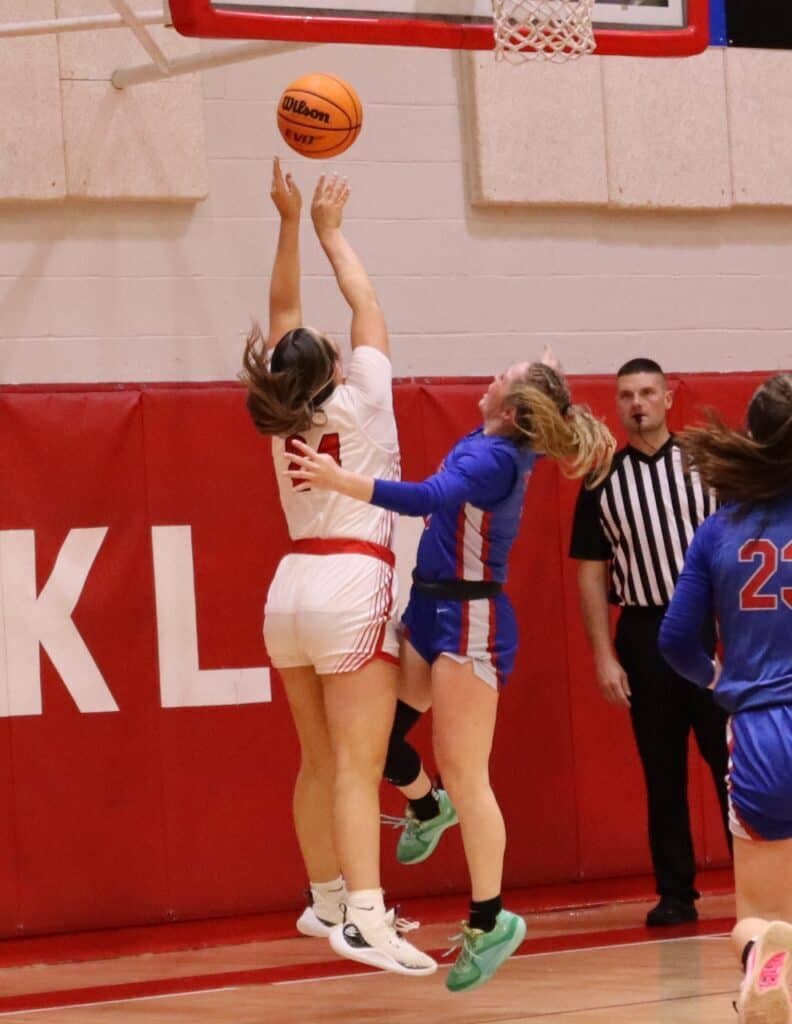 Female basketball players competing during a game, one jumping to shoot.