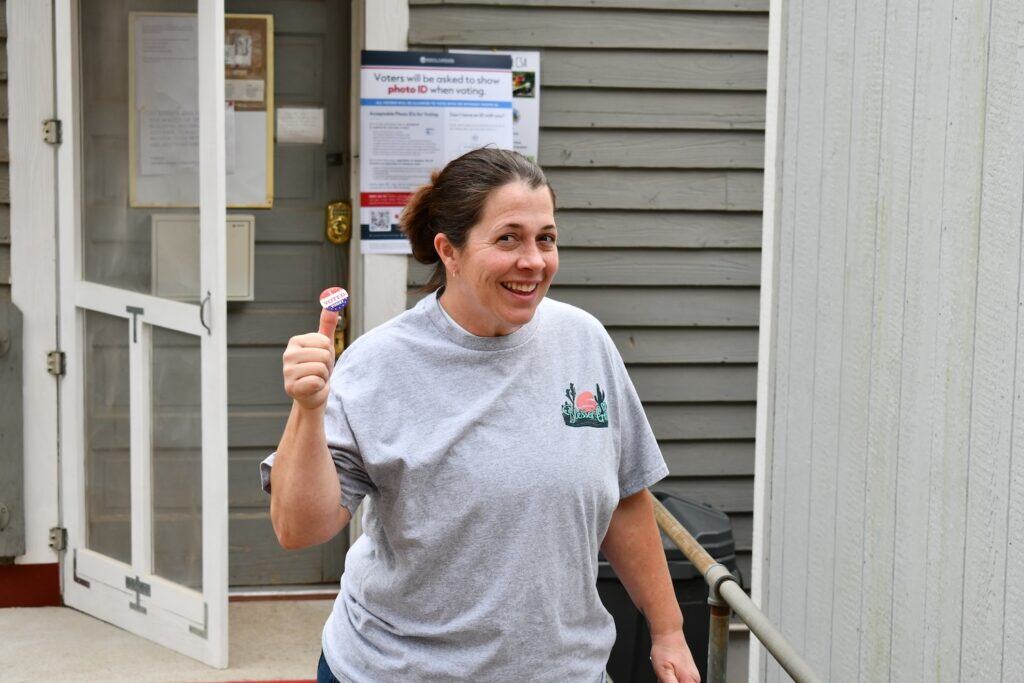Woman smiling and holding an election sticker outside polling station.