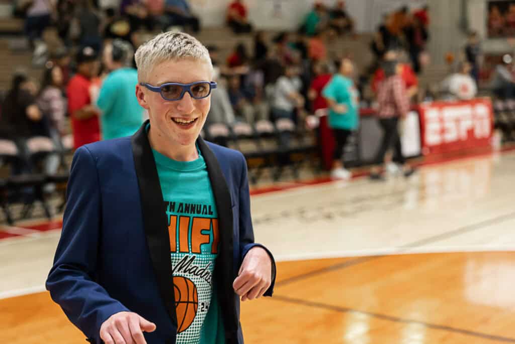 Young man smiling at FHS March Madness basketball event, packed gymnasium.