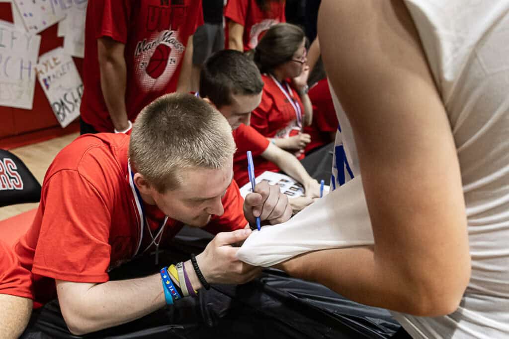 Students signing autographs at FHS March Madness event in a gymnasium.