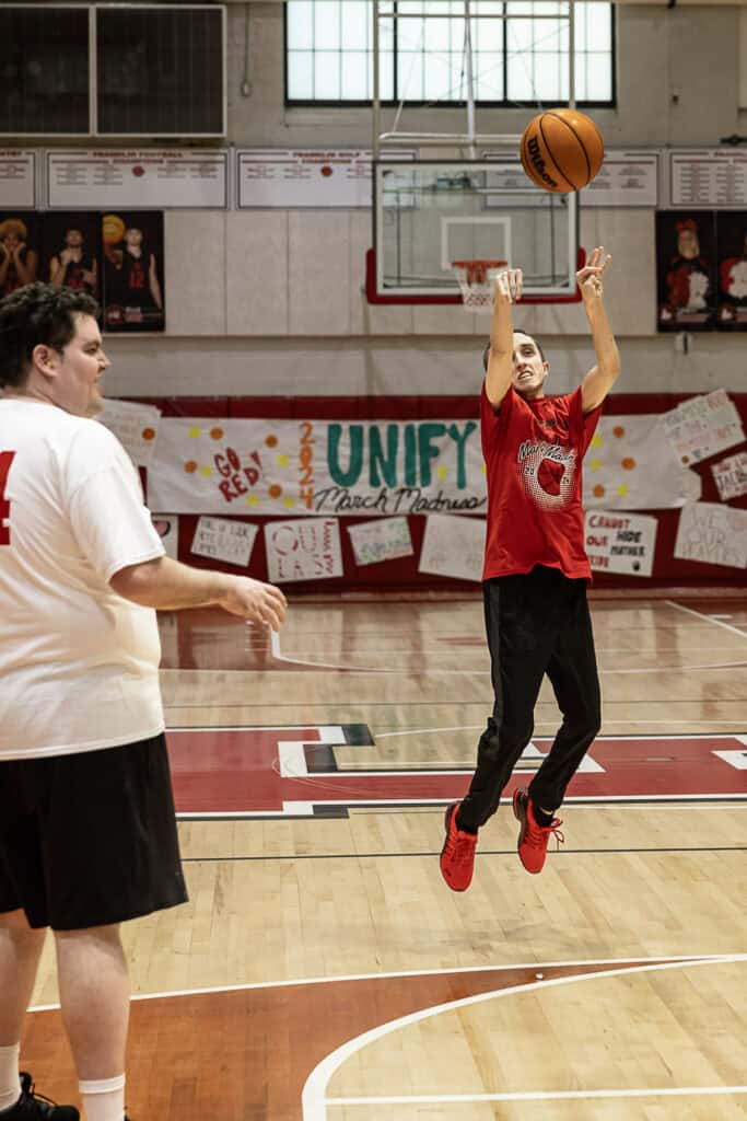 Student shooting basketball during FHS Unify March Madness event at gym.
