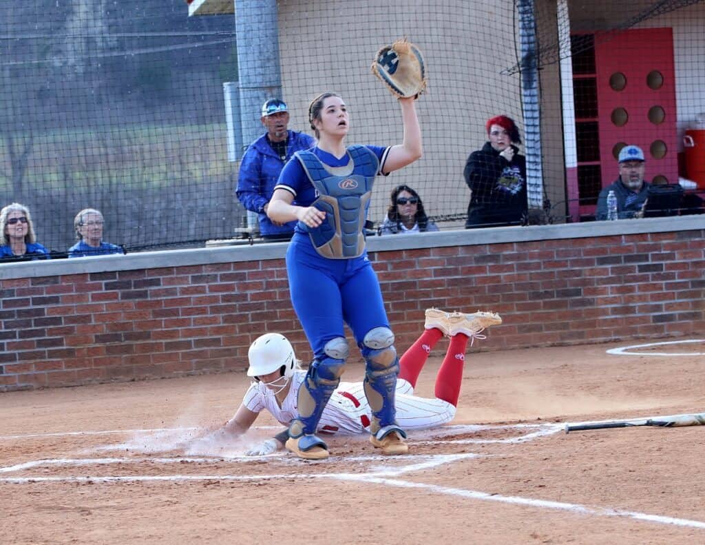 Female softball player sliding into home plate during game.