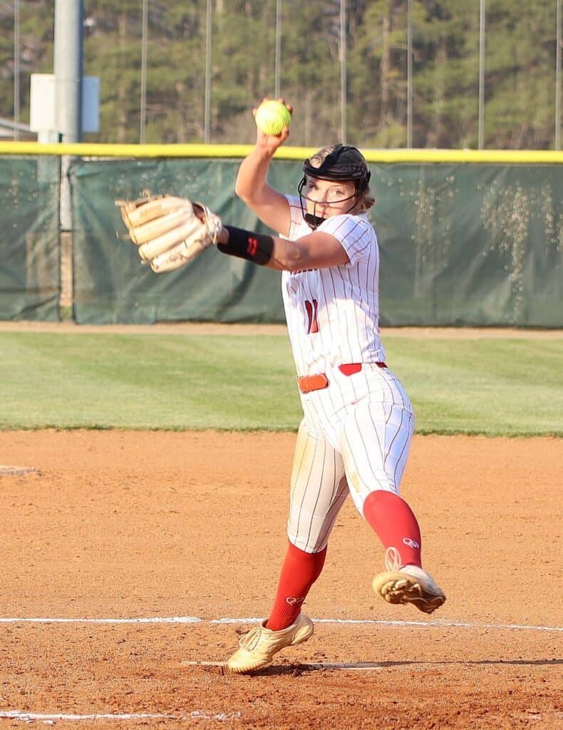 Female softball player pitching during game, breaking records, undefeated streak.
