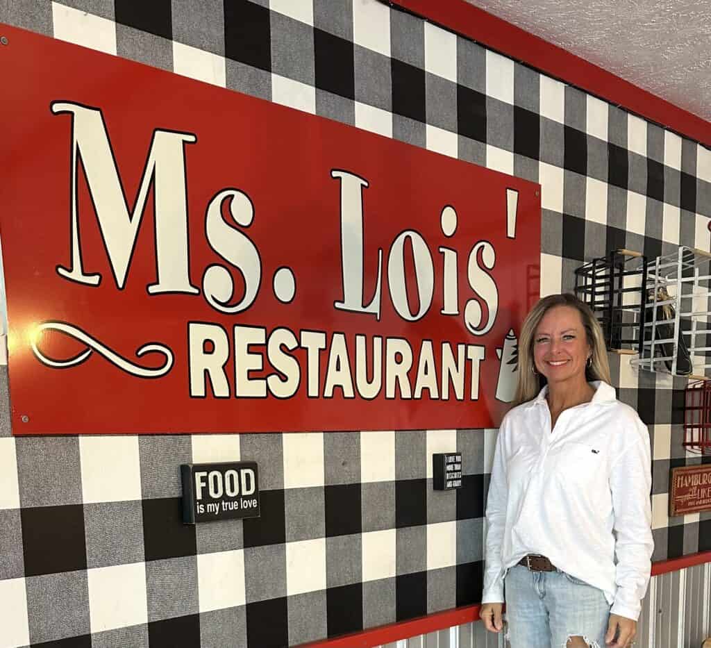 Ms. Lois’ Restaurant sign with a smiling woman in front, emphasizing food and family values.