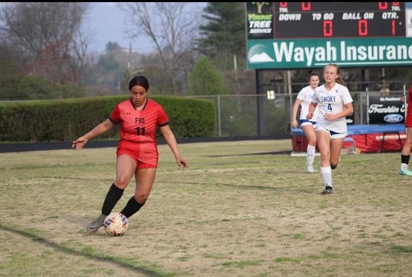 Female soccer player in red uniform kicking the ball during match.