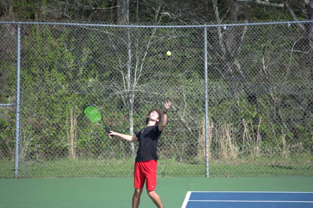 Young athlete practicing tennis serve on outdoor court.