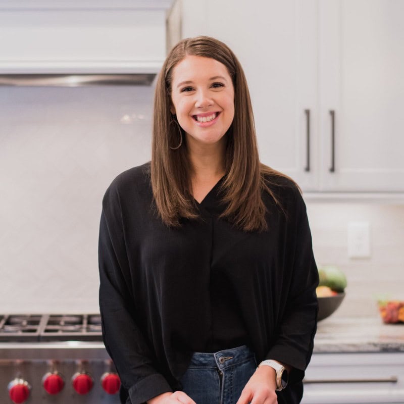 Smiling woman in a modern kitchen with fresh summer produce, promoting healthy eating.