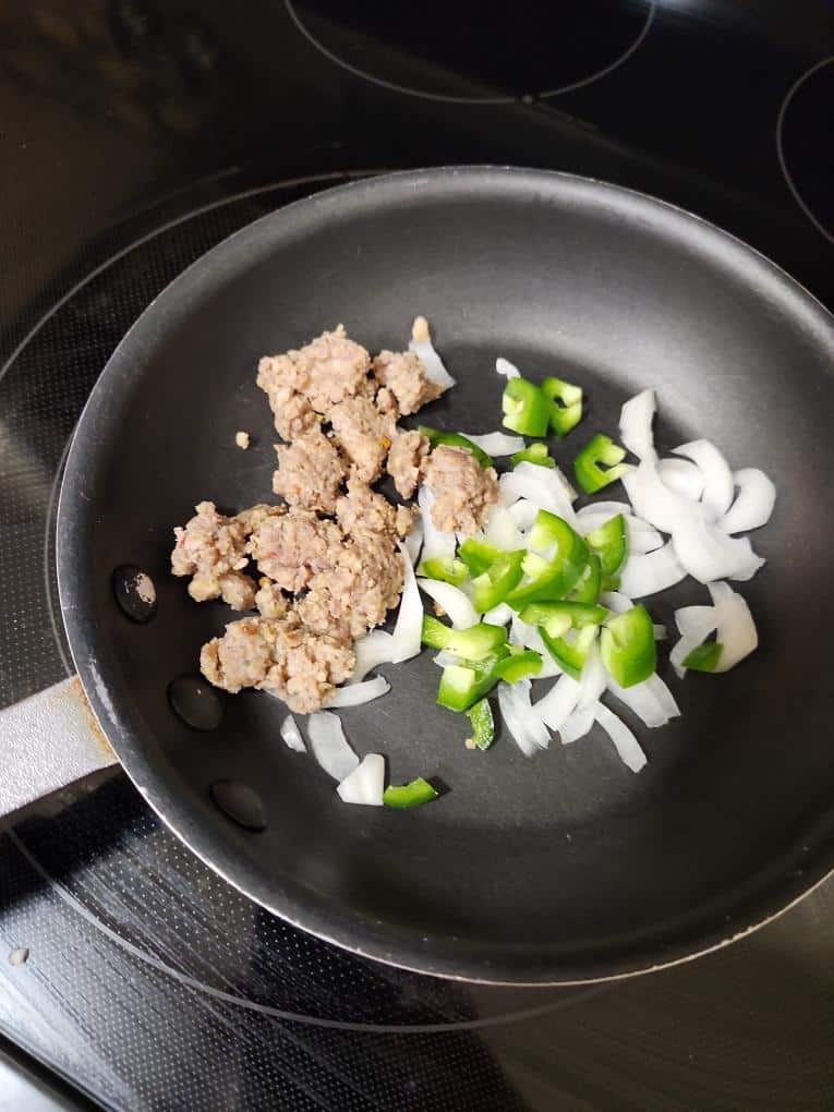 Sautéing ground sausage with chopped onions and green peppers in a frying pan for a fresh farm-to-ta.