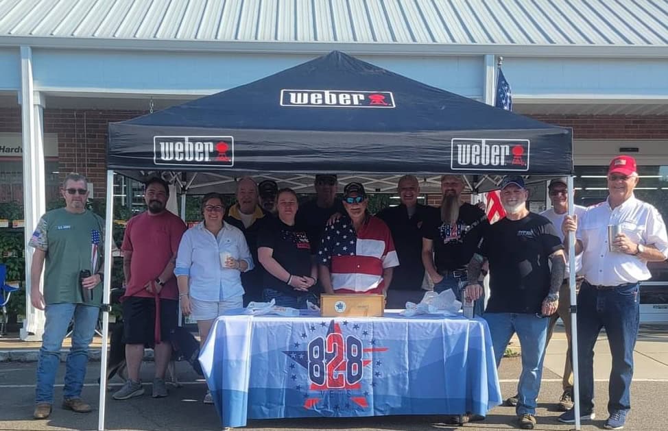 Group of people at Macon Sense BBQ event under Weber tent with American flags.