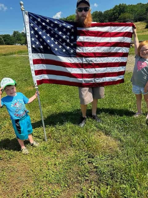 American flag held by a man with children on a sunny day.