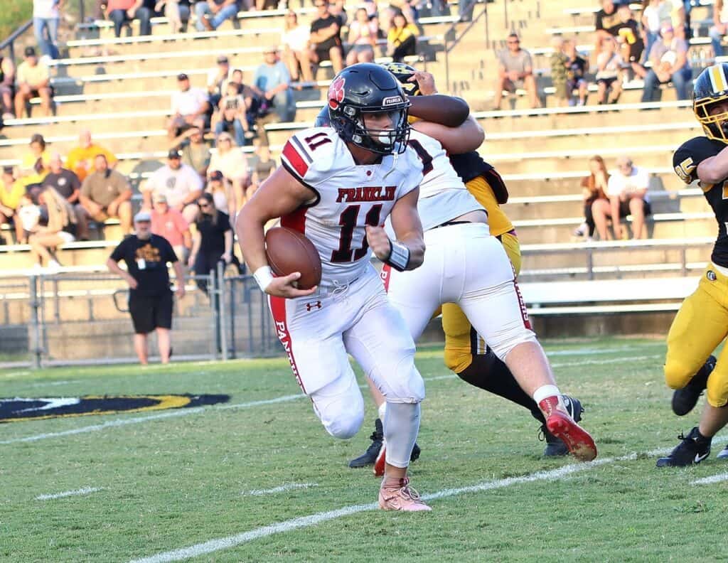 Football player running with ball during game, defenders in background.