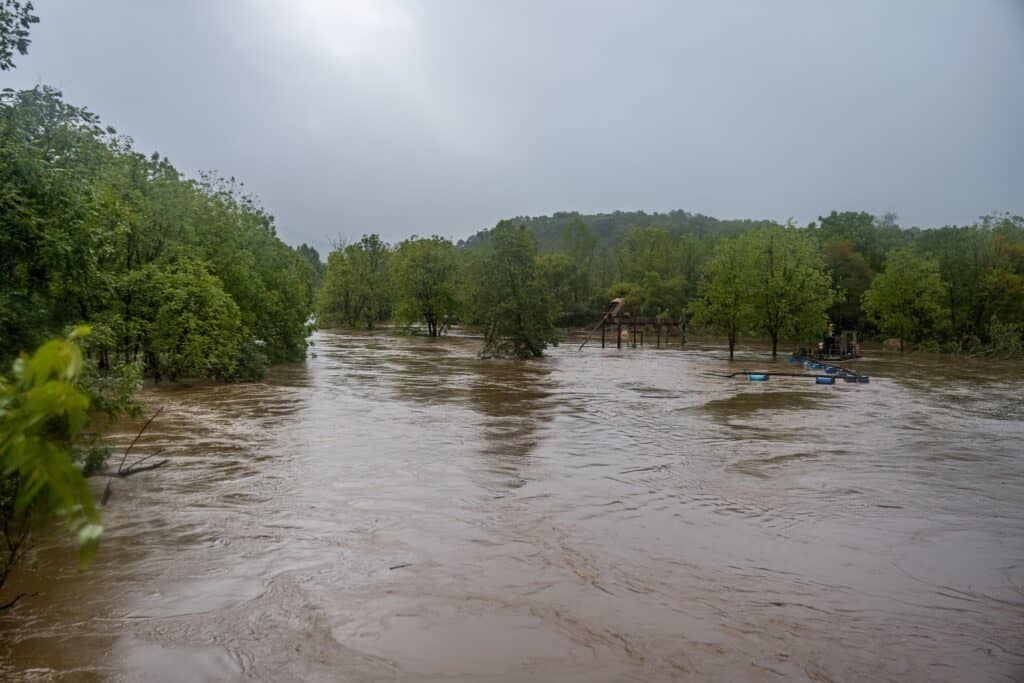 Flooded neighborhood with trees and a playground under cloudy sky.