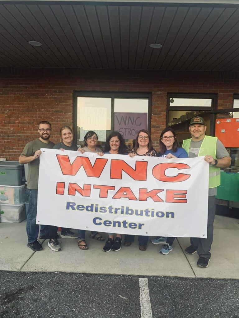 Group of volunteers holding WNC Intake Redistribution Center banner outside.