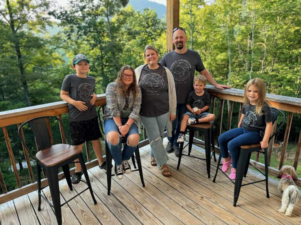 Family enjoying outdoor time on a wooden deck in a lush green forest.