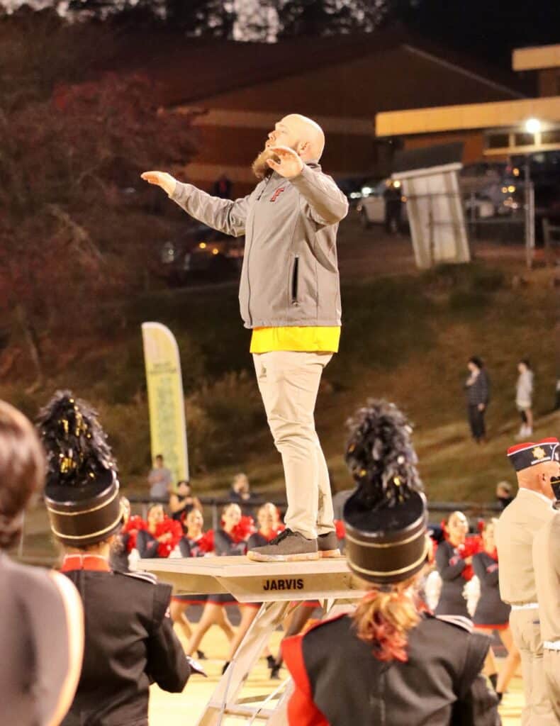 Band director conducting outdoor rehearsal with students during a performance.