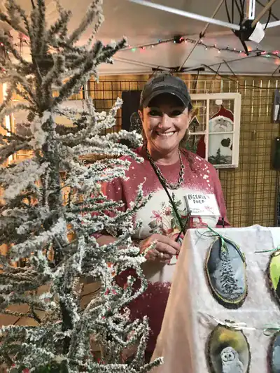 Woman at Macon Sense Christmas craft show with holiday decorations and handmade ornaments.