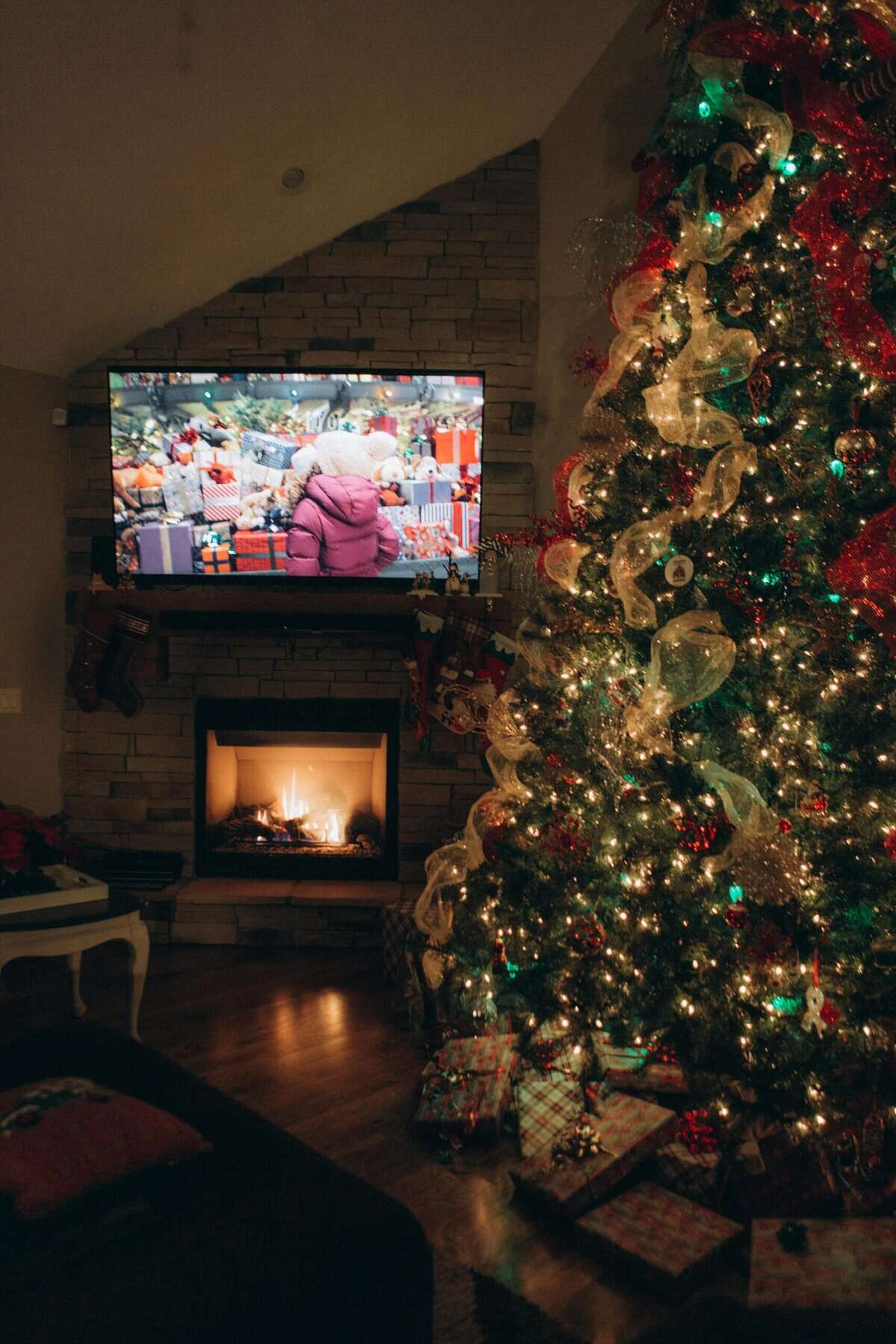 Christmas decorated tree with presents and a cozy fireplace scene.