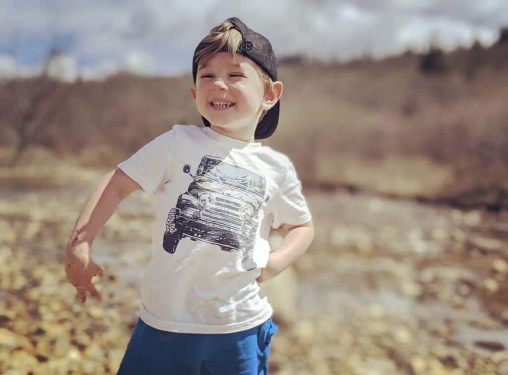 Child smiling and playing outdoors in a natural setting.