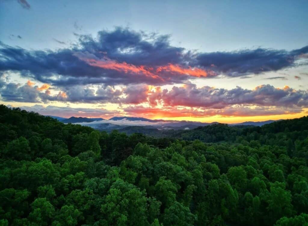 Sunset landscape with vibrant clouds over a dense green forest, capturing nature's beauty and tranqu.