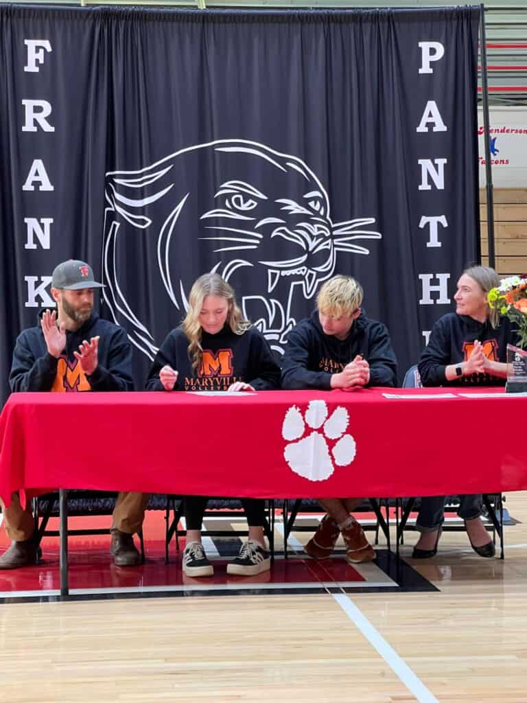 Young athletes signing college sports commitments at FHS event.