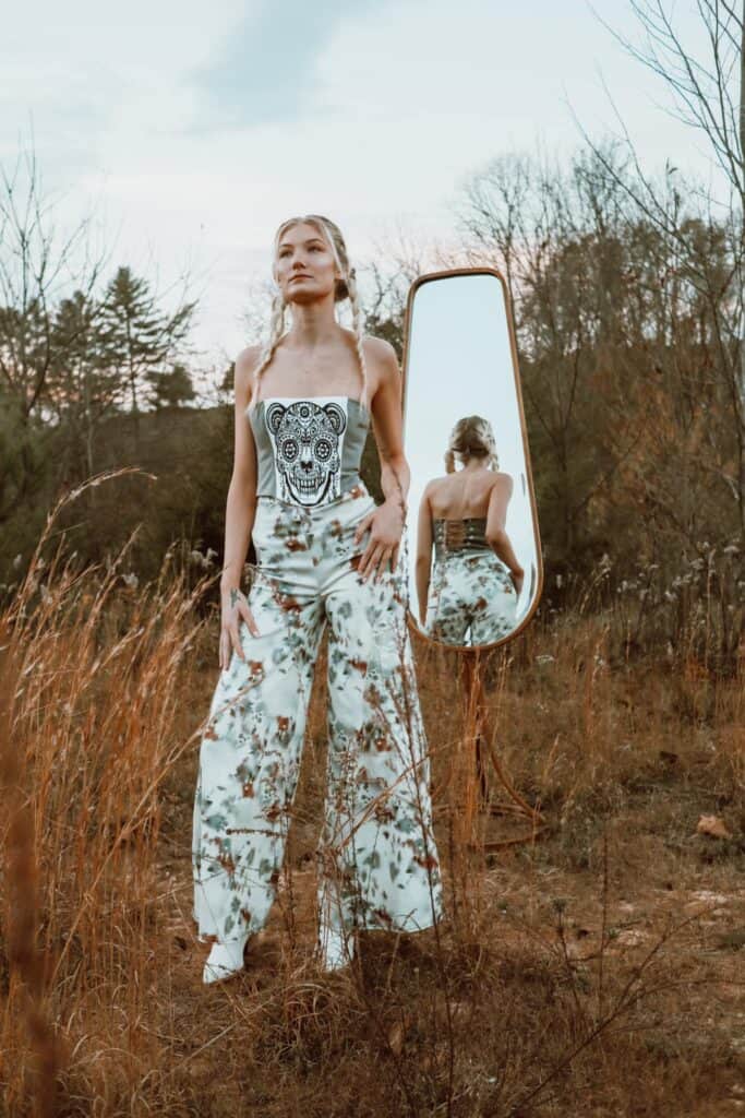 Fashion model standing outdoors with mirror, showcasing stylish outfit.