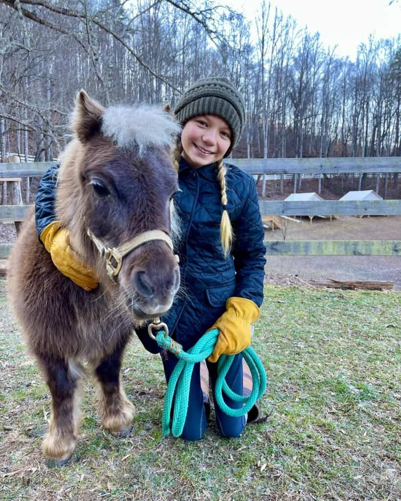 Young girl smiling with pony during equine therapy session outdoors.