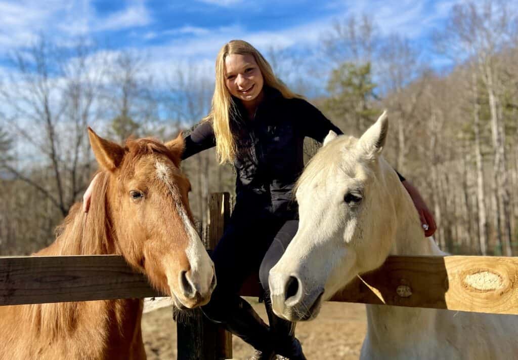 Woman riding horses in outdoor therapy session for veterans' emotional healing.