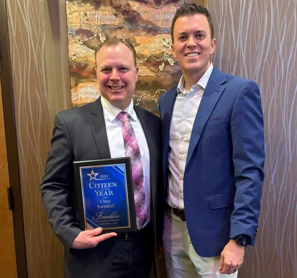 Two men at an award ceremony, one holding a Citizen of the Year plaque, celebrating community recogn.