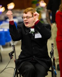Joyful young man in wheelchair celebrating at Night to Shine event.