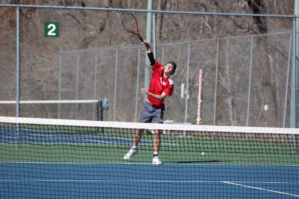 Young male tennis player serving on outdoor court during match.
