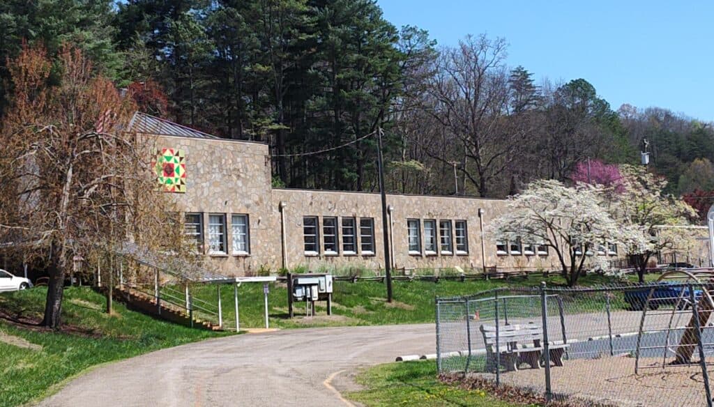 Cowee School building surrounded by trees and blooming flowers in spring.