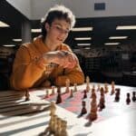 Young senior playing chess, awarded scholarship, in a library setting.