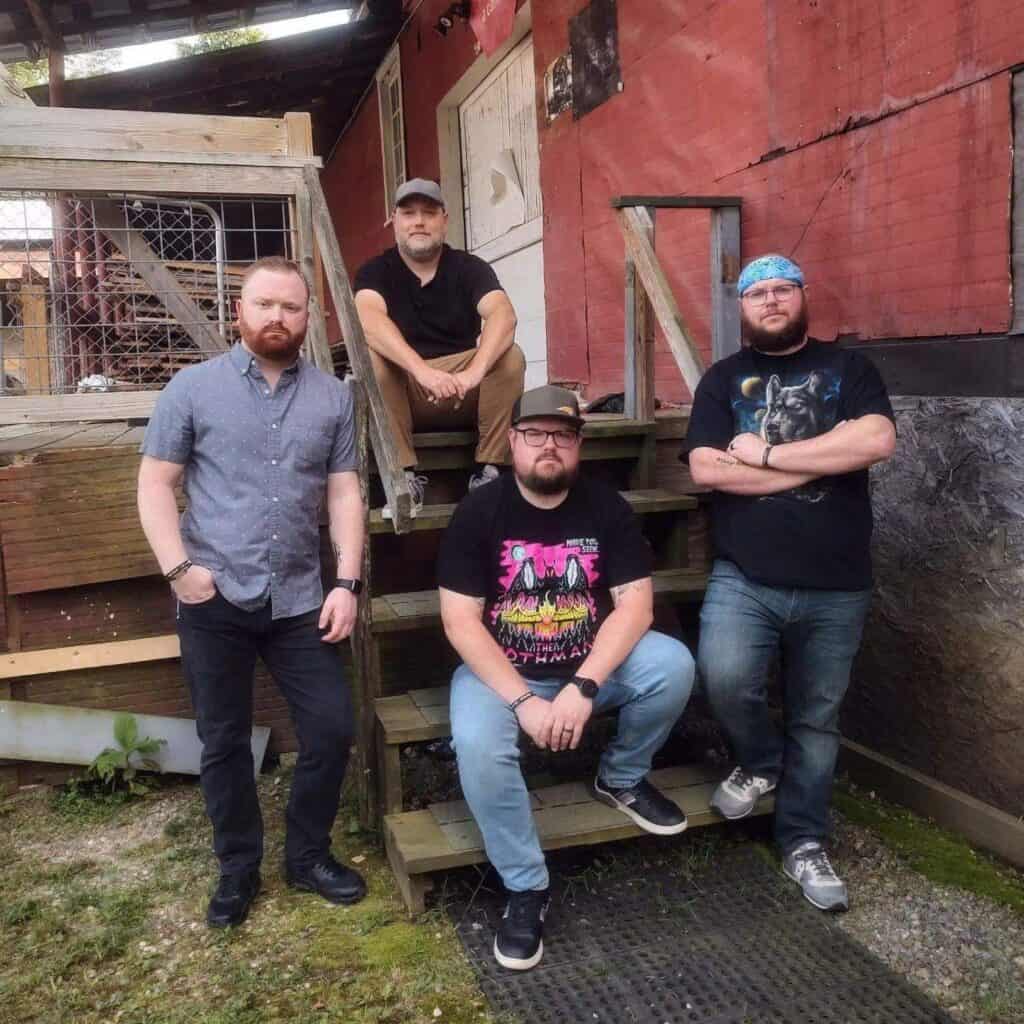 Four men posing on wooden stairs outside a rustic building, representing Macon Sense band.