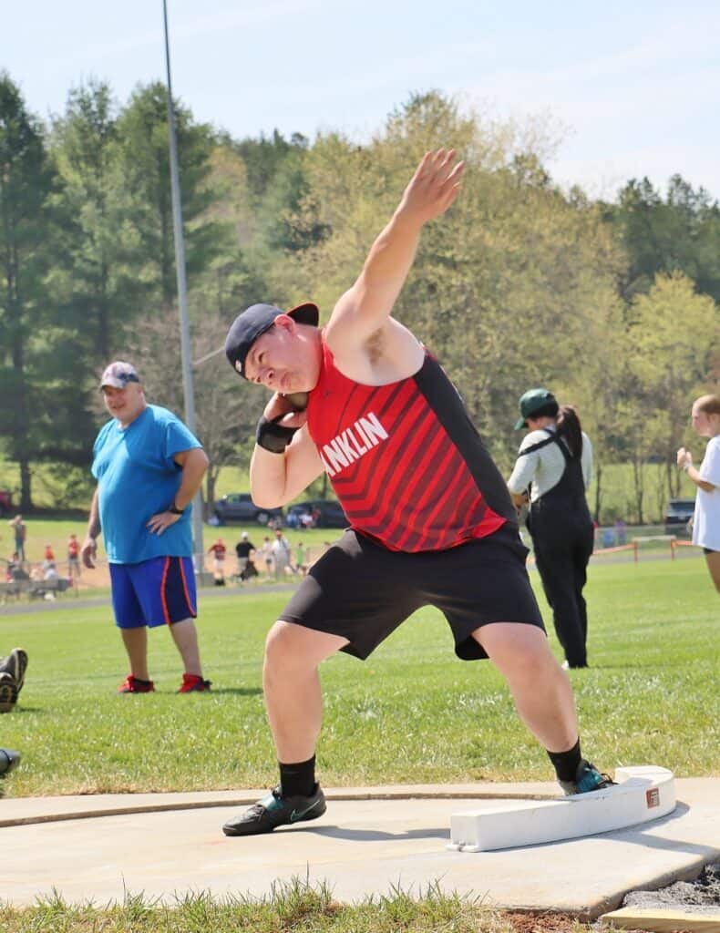 Young male athlete preparing for shot put at track meet.