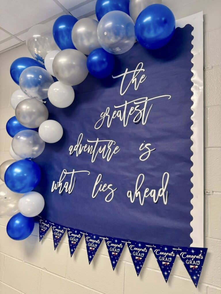 Graduation wall with blue, white, and silver balloons and inspirational quote.