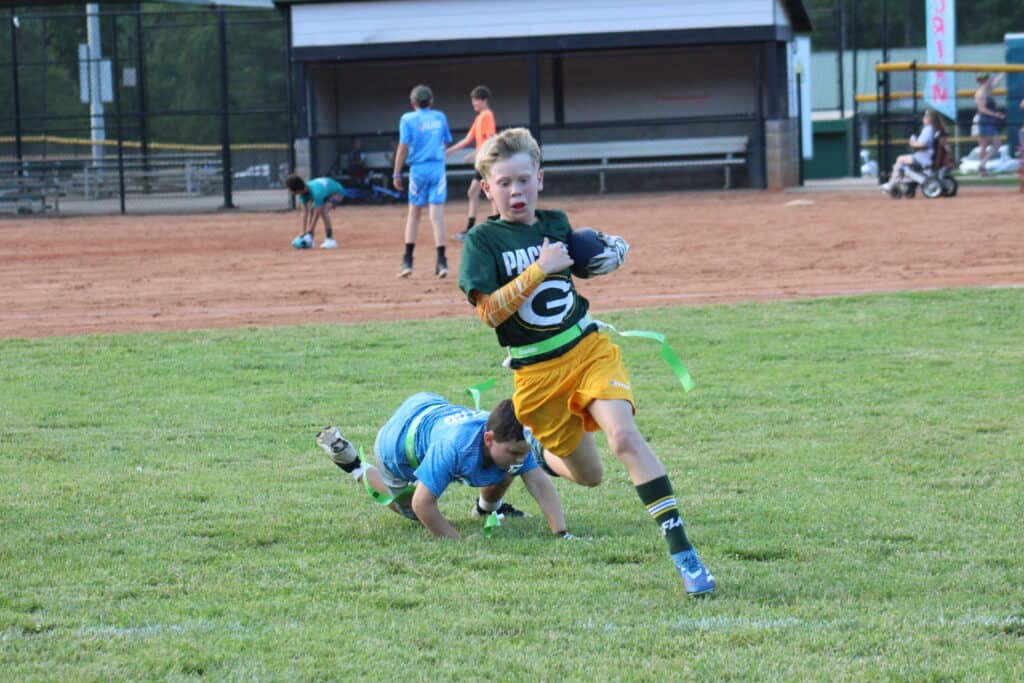 Young boy running with football during flag football game.