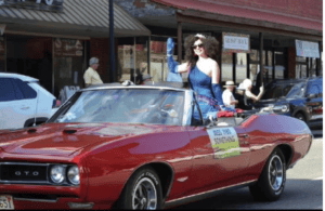 Woman riding in a vintage red convertible during Macon Sense event parade.