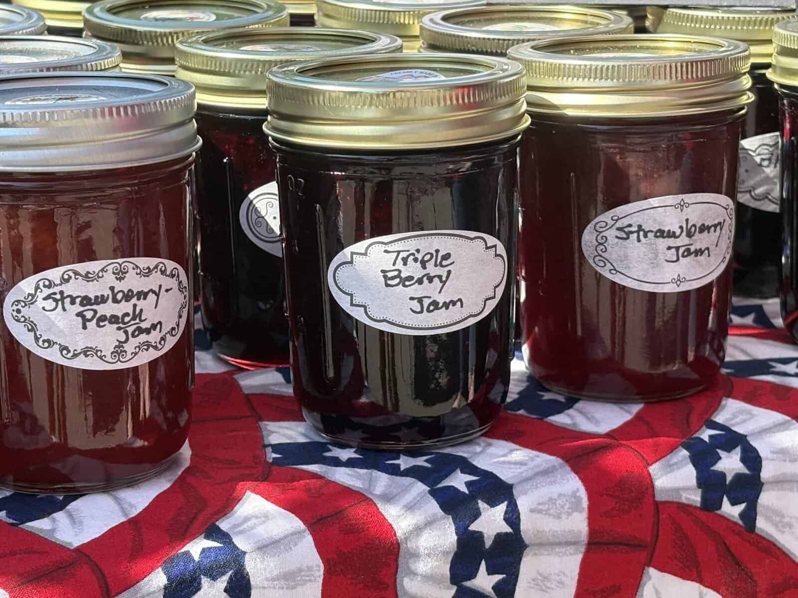 Assorted homemade strawberry, triple berry, and strawberry peach jams in jars.