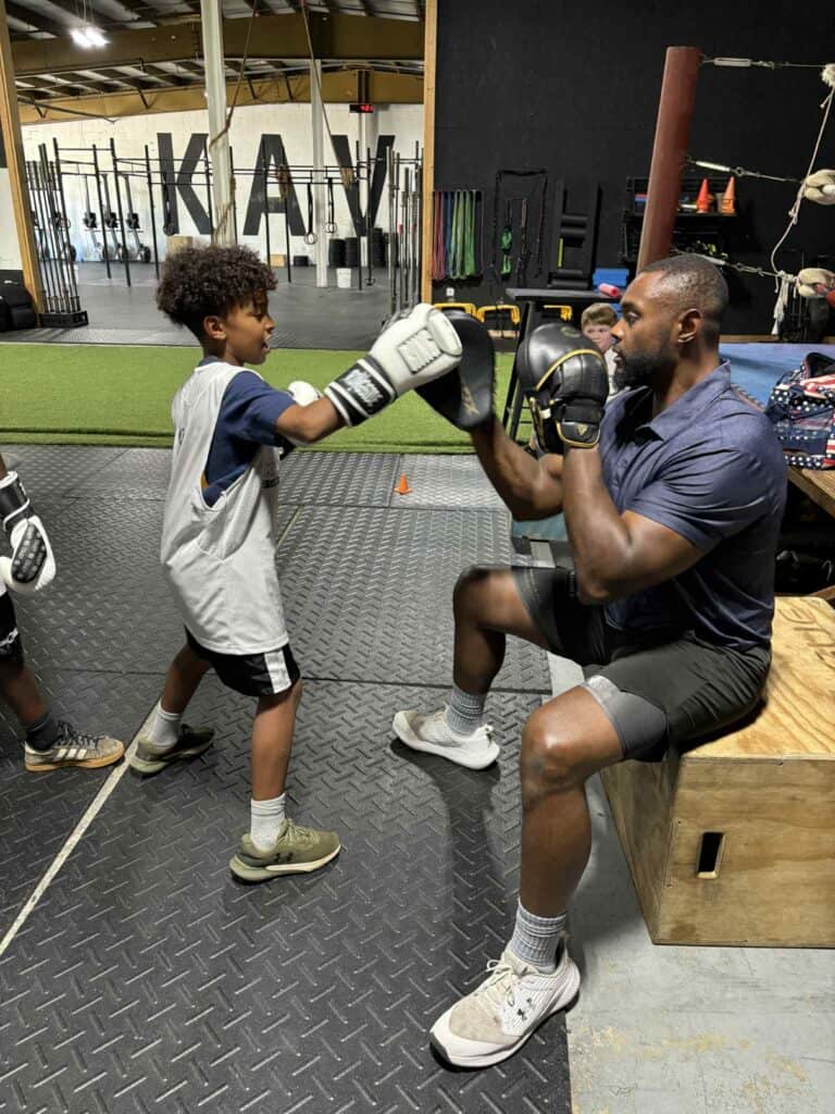 Young boy practicing boxing with coach in gym setting.