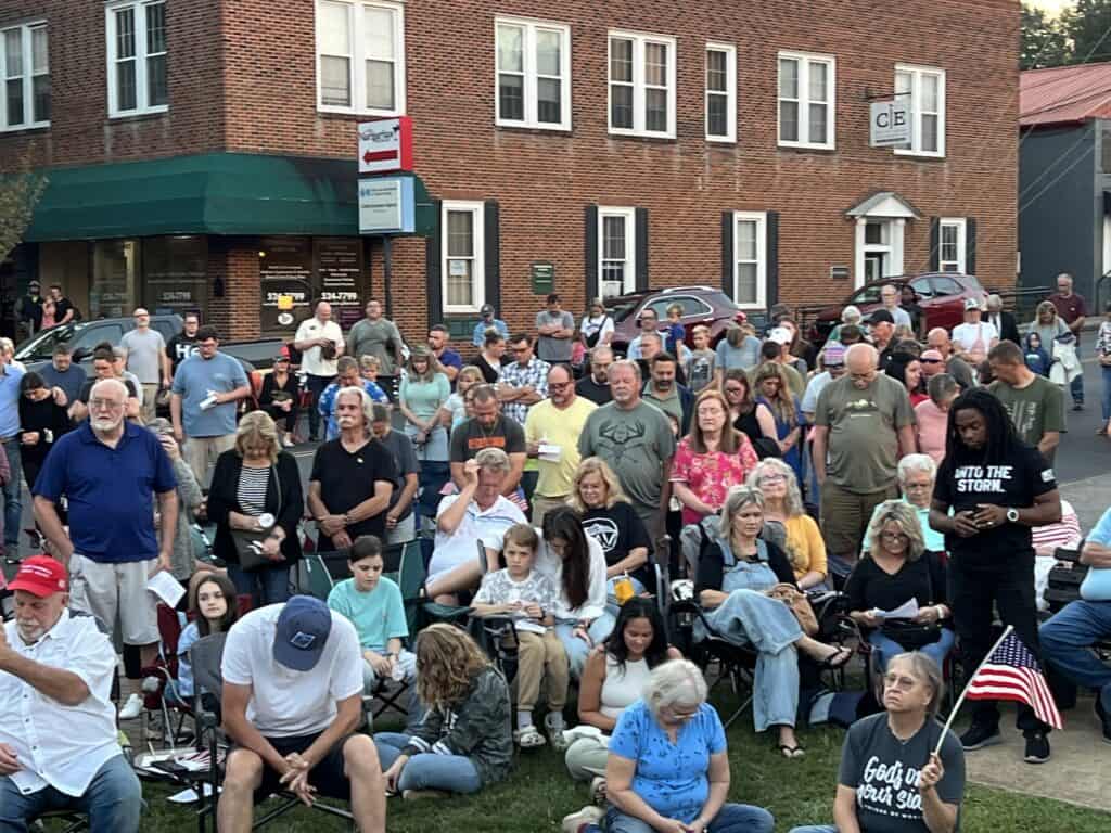 Crowd gathered outdoors praying for America during community event.